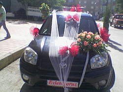 Siyah bir otomobilin kaputunda kırmızı gül düzenlemesi ve beyaz tül süsleme