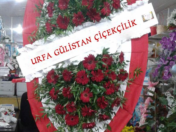 Kırmızı ve turuncu güllerden hazırlanmış ayaklı çelenk; kurdelesinde “Urfa Gülistan Çiçekçilik” yazıyor